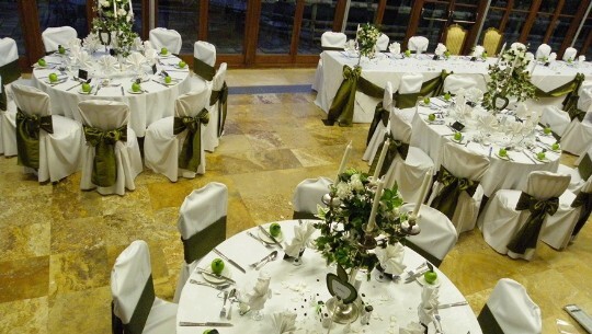 Interesting dark green theme with rich dark green bows on white chair covers and apples in centrepieces Craig y Nos Castle Wedding Venue Swansea Conservatory Wedding Breakfast Green and White Apple theme