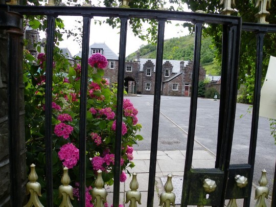 Looking through the wrought iron gates separating the theatre gardens from front courtyard, looking towards the gatehouse (far right) Craig y Nos Castle Wedding Venue Swansea Front Courtyard looking towards gatehouse and atrium accommodation