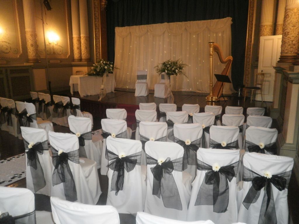 White chair covers in the theatre with grey/black sashes, note too the harp on stage in right corner Craig y Nos Castle Wedding Ceremony Room with white chair covers and harp on stage